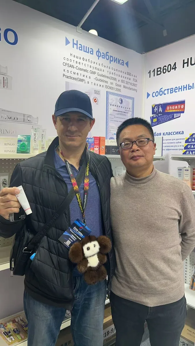 A buyer and Zongheng representative in front of an "Our factory" board listing SGS, GMP and ISO certifications