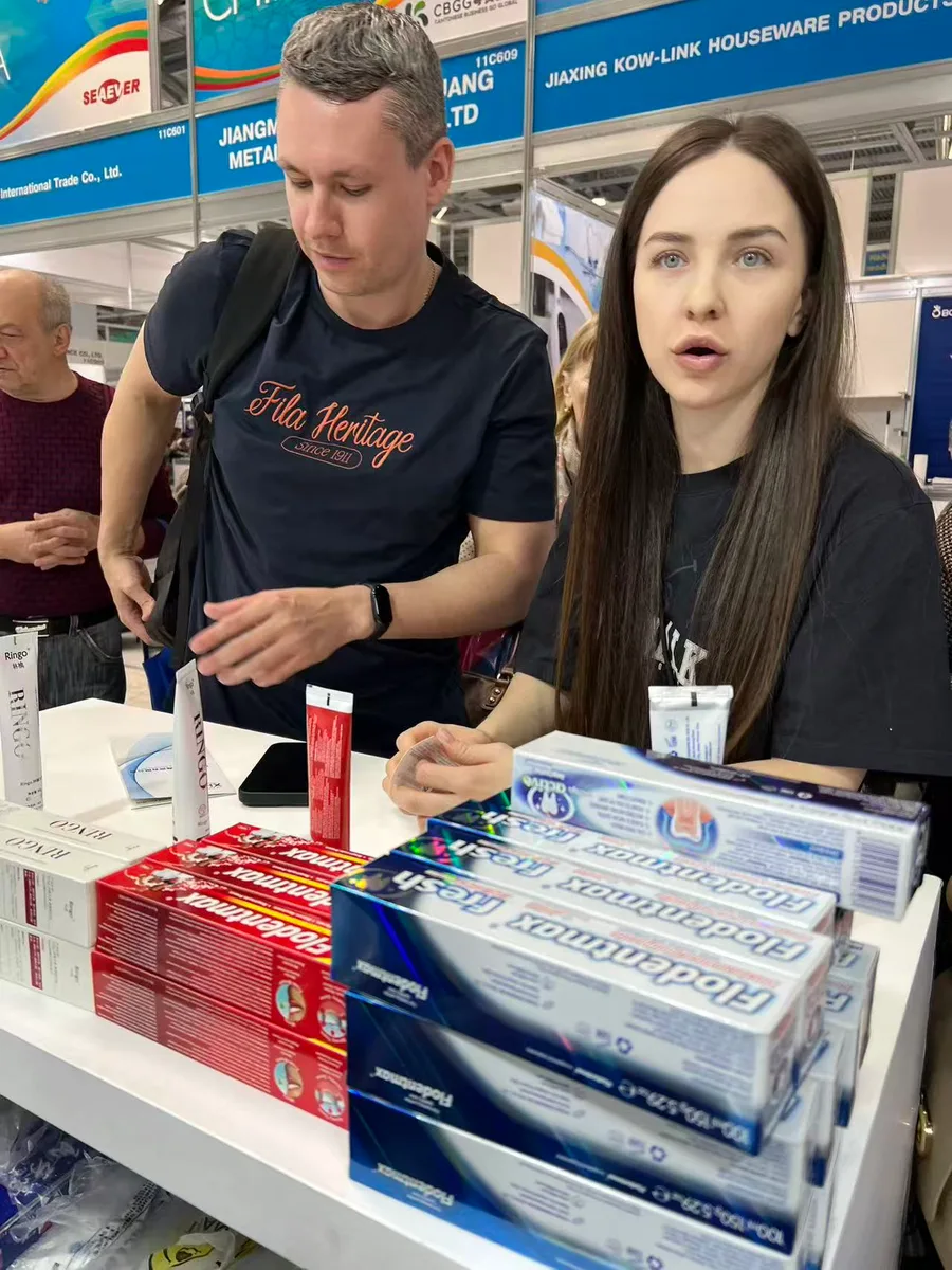 A Russian buyer holding a toothbrush while a Zongheng representative offers a business card at booth 11B604