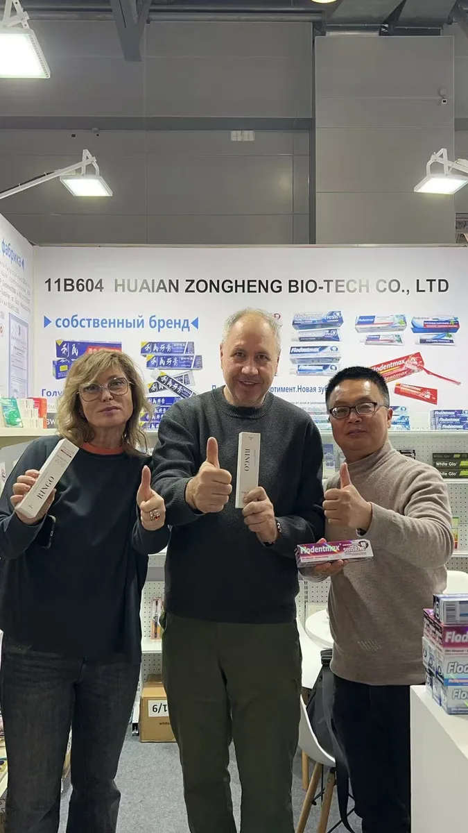 Two Russian buyers and a Zongheng sales representative giving a thumbs-up while holding toothpaste at the trade show booth